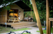 Familie geniet op het terras van een safaritent bij Urban-Gardens Ieper, omringd door natuur.