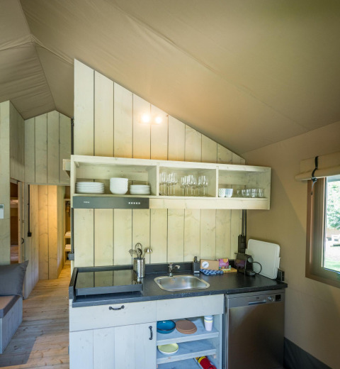 Zona de cocina en la Family Glampingtent de Urban-Gardens Ieper, Bélgica, con estantes y fregadero.