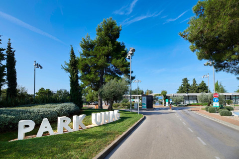 Entrada al Camping Park Umag en Istria, Croacia, rodeada de árboles y cielo azul despejado.