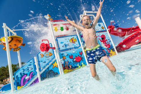 Un bambino si diverte e spruzza acqua nel parco acquatico colorato di Camping Park Umag, Istria, Croazia.