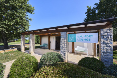 Lavanderia all'aperto al Camping Park Umag in Istria, Croazia, con insegna e panchina sotto la tettoia.