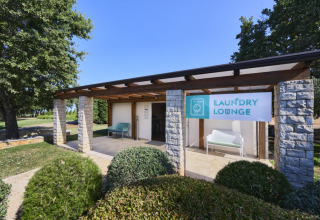 Udendørs vaskelounge ved Camping Park Umag i Istrien, Kroatien, med skilt og bænk under halvtag.