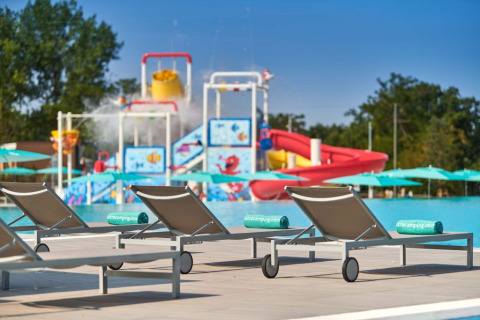 Liegestühle am Pool im Camping Park Umag, mit Wasserrutschen und Spielplatz im Hintergrund, Istrien, Kroatien.