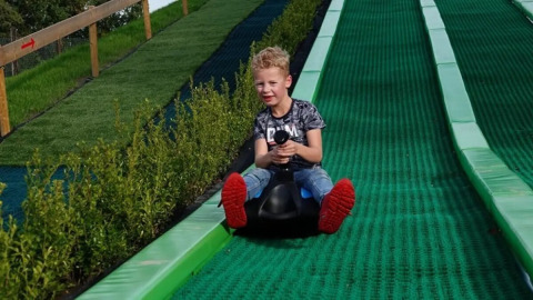 Boy enjoys riding down a green slide at The HappyFarm holiday park in Gelderland, Netherlands.