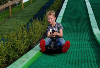 Jongen glijdt van groene baan bij The HappyFarm, een vakantiepark in Gelderland, Nederland.