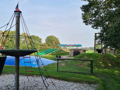 Udendørs legeplads og vandrutsjebaner på The HappyFarm-feriepark i Gelderland, Holland, under en blå himmel.
