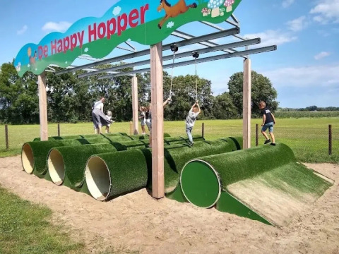 Kinderen spelen op een speeltoestel met groene buizen en touwen bij The HappyFarm in Gelderland, Nederland.