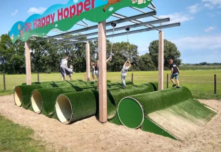 Kinder spielen auf einem Spielplatz mit grünen Röhren und Seilen im Ferienpark The HappyFarm in Gelderland.