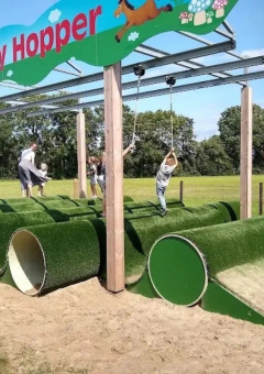 Børn leger på en legeplads med grønne rør og rebstropper i The HappyFarm feriepark i Gelderland, Holland.