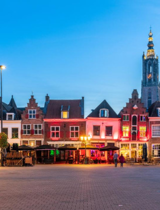 Aftenbillede af et farverigt oplyst torv med historiske bygninger og et kirketårn i Terschuur, Gelderland.