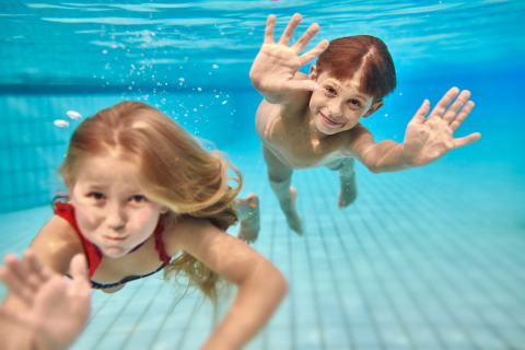 Twee kinderen zwemmen en glimlachen onder water in het zwembad van Camping Terme Catez in Slovenië.