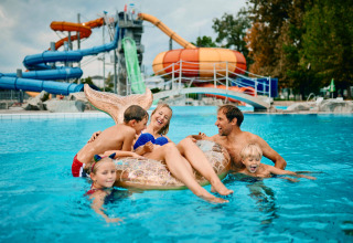 Familie nyder en dag i poolen på Camping Terme Catez-feriepark med farverige vandrutsjebaner i baggrunden.