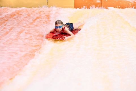 Enfant avec lunettes de natation bleues glissant sur planche rouge à Camping Terme Catez, Slovénie.