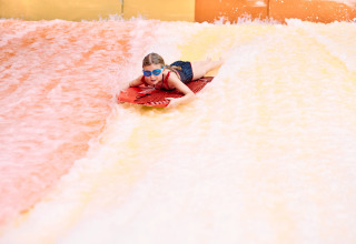 Bambino con occhialini blu scivola su tavola rossa allo scivolo d'acqua al Camping Terme Catez, Slovenia.