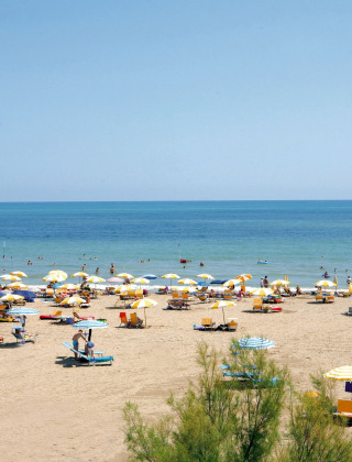 Playa con sombrillas amarillas y blancas y turistas en Camping Union Lido Mare, Véneto, Italia, en un día soleado.