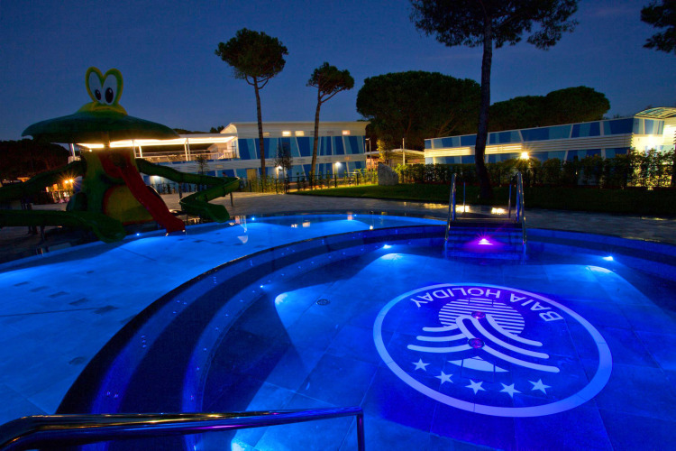 Verlichte zwembad en glijbaan bij Camping Village Cavallino, vakantiepark in Veneto, Italië, 's avonds.