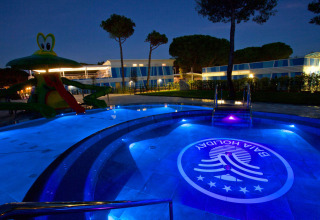 Piscina iluminada y tobogán acuático en Camping Village Cavallino, parque vacacional en Véneto, Italia, de noche.