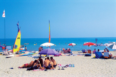 Playa en Camping Village Cavallino, parque de vacaciones en Véneto, Italia, con sombrillas y bañistas.