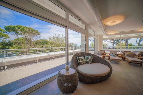 Área de salón luminosa y moderna con grandes ventanas, terraza y vistas a los árboles en Camping Village Cavallino.