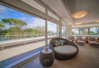 Area lounge moderna e luminosa con grandi finestre e vista su terrazza e alberi al Camping Village Cavallino.