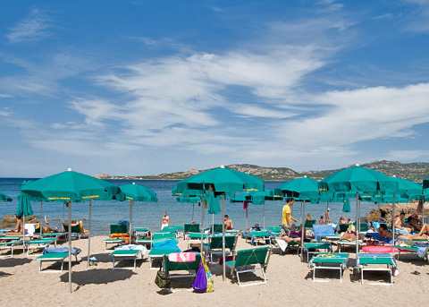 Escena de playa con sombrillas verdes y tumbonas en Centro Vacanze Isuledda, parque vacacional en Cerdeña, Italia.