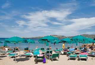 Strandscène met groene parasols en ligstoelen in Centro Vacanze Isuledda vakantiepark op Sardinië, Italië.