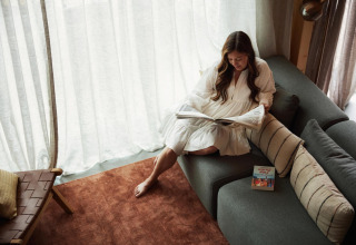 Mujer leyendo un periódico en el sofá de Unbrick One, una tiny house en Brinckerduyn, Países Bajos.