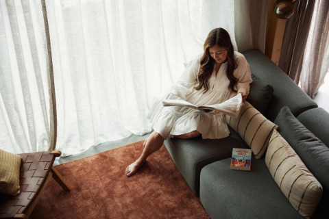 Woman reading a newspaper on a modern sofa in Unbrick One, Brinckerduyn, Netherlands, with soft sunlight.