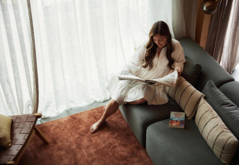 Woman reading a newspaper on a modern sofa in Unbrick One, Brinckerduyn, Netherlands, with soft sunlight.