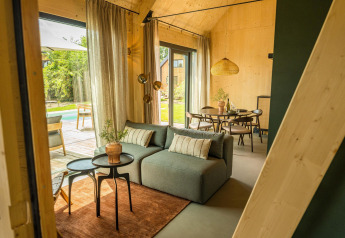 Interno luminoso di tiny house Unbrick One a Brinckerduyn, con divano, tavolo da pranzo e vista giardino.