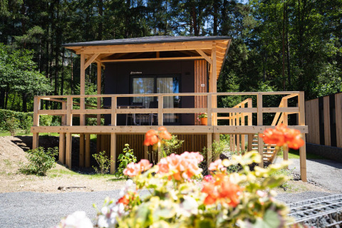 Cabaña Edelweiss de madera con terraza amplia, rodeada de naturaleza y flores coloridas en primer plano.