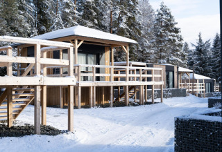 Lodges in legno innevati all'Edelweiss presso il lago Ossiacher, Austria, circondati da pini in inverno.