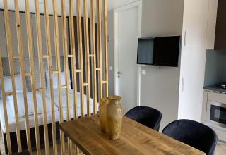 Moderne Edelweiss lodge met houten afscheiding, eettafel, vazen, tweepersoonsbed, tv en kitchenette.