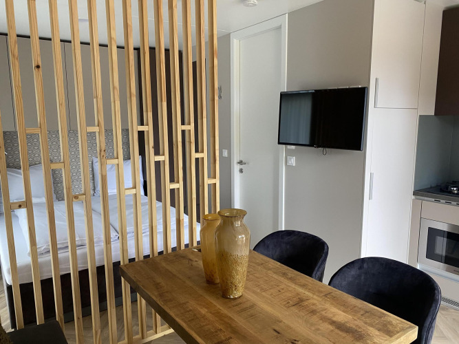 Moderne Edelweiss lodge met houten scheiding, eettafel, vazen, tweepersoonsbed, tv en keukenhoek.