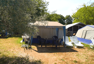 Holiday park in Istria, Croatia, featuring tents, sun loungers, and outdoor chairs under green trees.