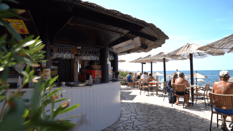 Außenbar mit Strohdach und Gästen an Tischen am Strand im Camping Zelena Laguna, Istrien, Kroatien.