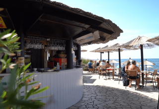 Udendørs bar med stråtag og gæster ved borde nær stranden på Camping Zelena Laguna, Istrien, Kroatien.