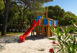 Aire de jeux avec toboggan rouge et sable, entourée d’arbres au Camping Zelena Laguna en Istrie, Croatie.