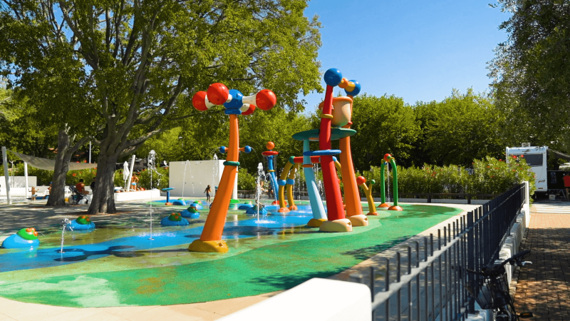 Aire de jeux aquatique colorée pour enfants au Camping Zelena Laguna, entourée d’arbres et de soleil.
