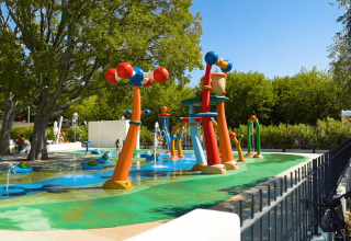 Colorido parque acuático infantil en Camping Zelena Laguna, rodeado de árboles y cielo soleado.