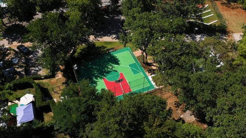 Luchtbeeld van een basketbalveld omringd door bomen in Camping Zelena Laguna, Istrië, Kroatië op een zonnige dag.