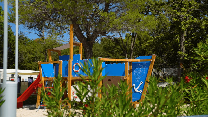 Speeltuin met houten schip in blauw, omgeven door groen, op Camping Zelena Laguna in Istrië, Kroatië.