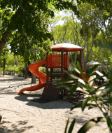 Parque infantil con toboganes y juegos bajo árboles en Camping Zelena Laguna, Istria, Croacia.