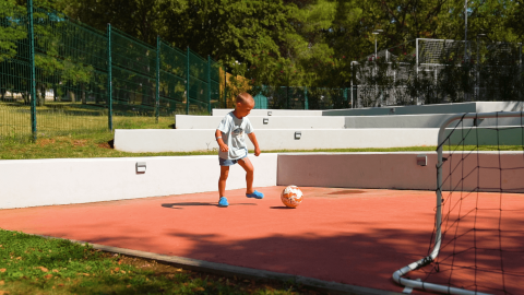 Ein Kind spielt Fußball auf dem Gelände des Camping Zelena Laguna in Istrien, Kroatien, bei Sonnenschein.