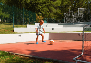 Et barn spiller fodbold på Camping Zelena Laguna i Istrien, Kroatien, omgivet af grønne træer og hegn.