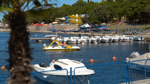 Barche, pedalò e turisti rilassati al porto turistico del Camping Zelena Laguna, Istria, Croazia.