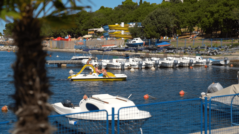 Boats, pedalos and tourists relaxing at the marina in Camping Zelena Laguna holiday park, Istria, Croatia.