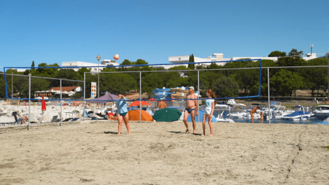 Menschen spielen Beachvolleyball im Camping Zelena Laguna, Istrien, Kroatien, mit Zelten und Booten im Hintergrund.