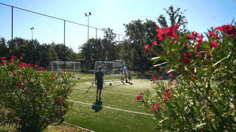 Menschen spielen Fußball auf einem sonnigen Spielfeld mit Blumen in Camping Bijela Uvala, Istrien, Kroatien.