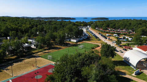 Vista aérea de Camping Bijela Uvala en Istria, Croacia con canchas deportivas, caravanas y el mar al fondo.